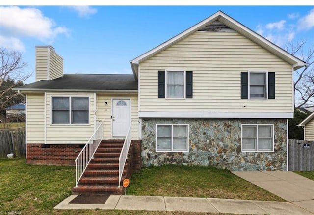 split level home featuring a front yard, fence, stone siding, and a chimney