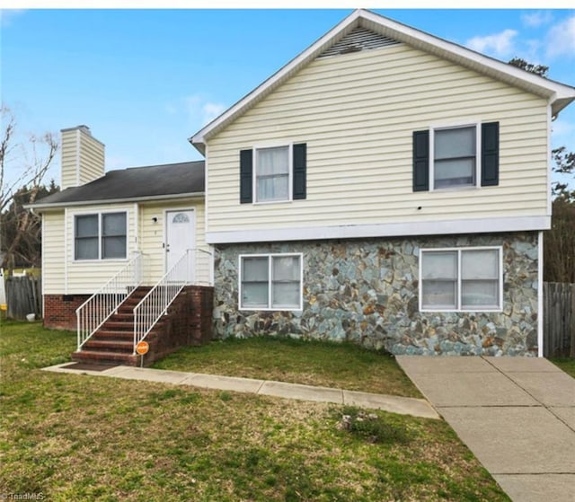 split level home with stone siding, a chimney, a front yard, and fence