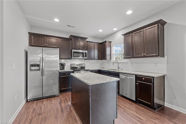 kitchen with light stone counters, a kitchen island, dark hardwood / wood-style flooring, stainless steel appliances, and sink