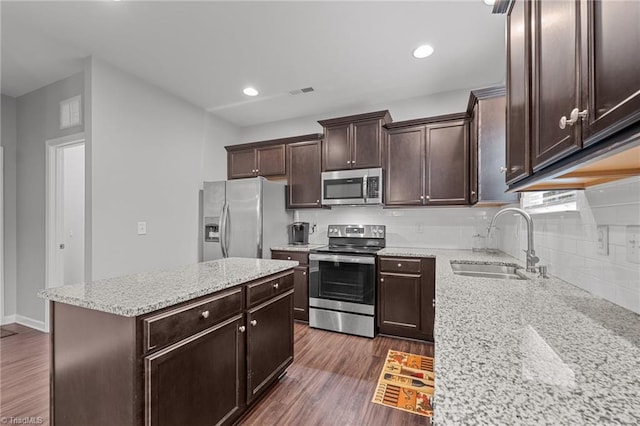 kitchen with appliances with stainless steel finishes, light stone countertops, dark hardwood / wood-style flooring, a center island, and sink