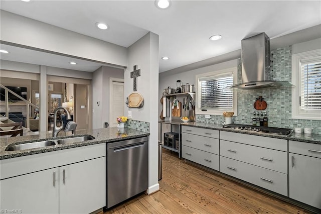 kitchen with white cabinetry, appliances with stainless steel finishes, light wood-type flooring, wall chimney range hood, and sink