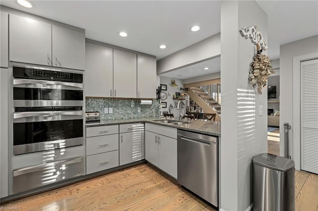 kitchen with appliances with stainless steel finishes, decorative backsplash, dark stone counters, light hardwood / wood-style flooring, and sink