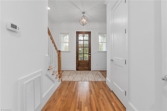 entrance foyer featuring visible vents, baseboards, stairway, ornamental molding, and light wood-style flooring