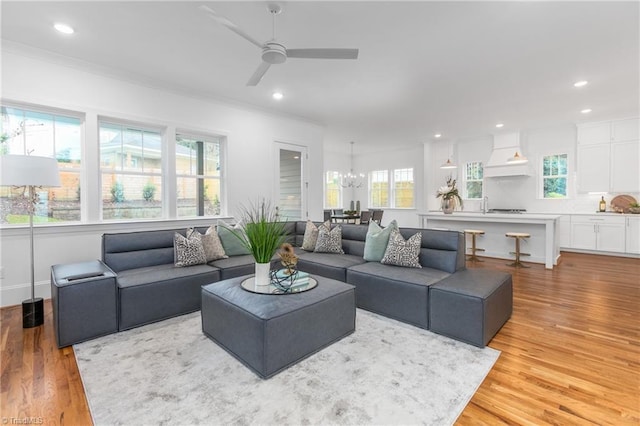 living area with recessed lighting, light wood-style flooring, ceiling fan with notable chandelier, and ornamental molding