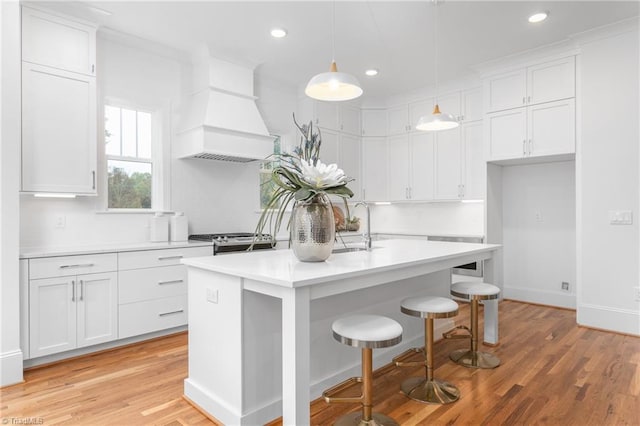 kitchen featuring stainless steel range with gas stovetop, light countertops, custom range hood, white cabinets, and a sink