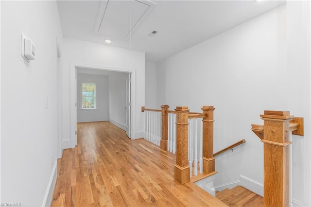 hallway with baseboards, visible vents, attic access, light wood-style flooring, and an upstairs landing