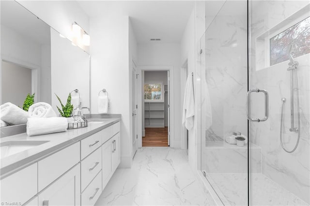 bathroom with a marble finish shower, marble finish floor, double vanity, and a sink