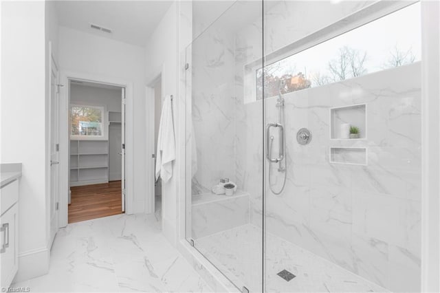 bathroom featuring visible vents, a walk in closet, marble finish floor, a marble finish shower, and vanity