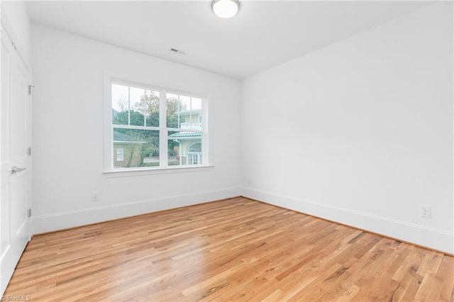 empty room with light wood finished floors, visible vents, and baseboards