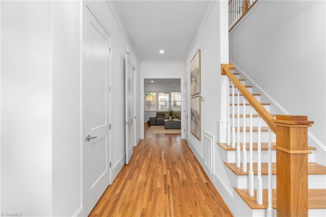 hallway featuring light wood-type flooring, visible vents, ornamental molding, and stairway