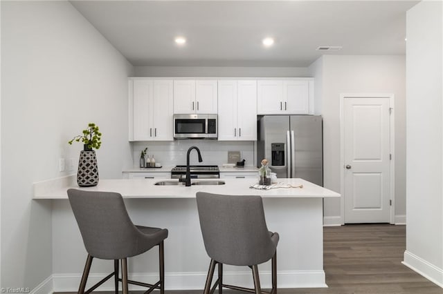 kitchen with white cabinetry, appliances with stainless steel finishes, a kitchen breakfast bar, dark wood-type flooring, and decorative backsplash