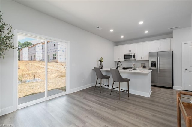 kitchen featuring stainless steel appliances, kitchen peninsula, a kitchen breakfast bar, white cabinetry, and light hardwood / wood-style flooring