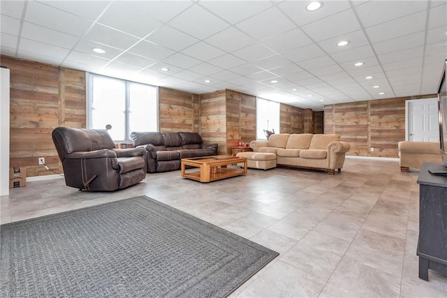 living room featuring a drop ceiling and wooden walls