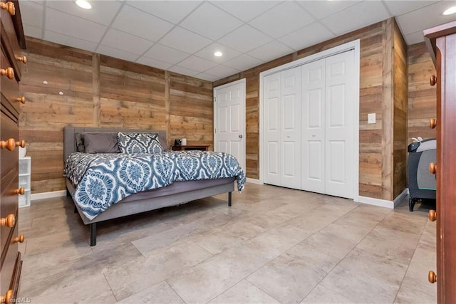 bedroom with wooden walls, a closet, and a drop ceiling