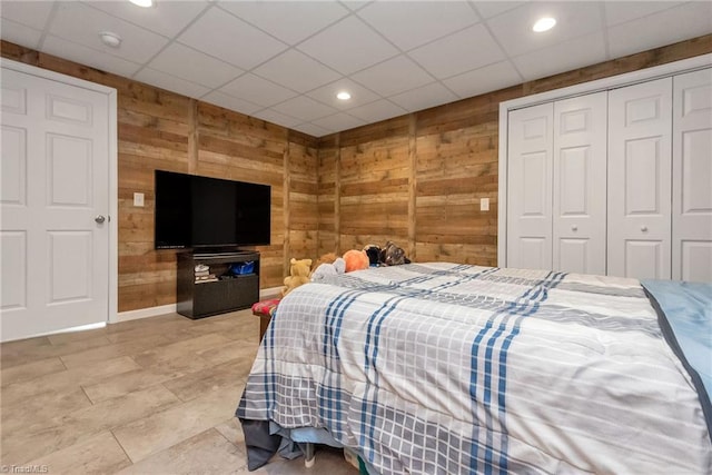 bedroom with a paneled ceiling, wooden walls, and a closet