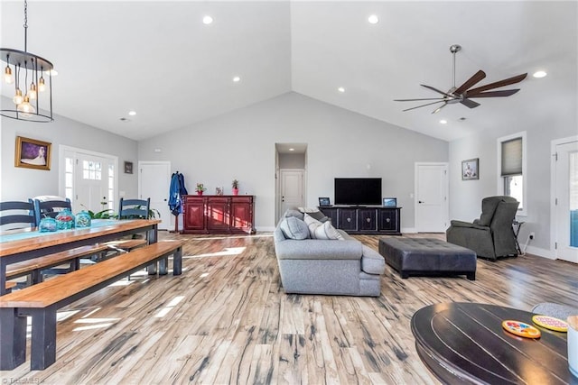 living room featuring ceiling fan with notable chandelier, light hardwood / wood-style floors, and vaulted ceiling