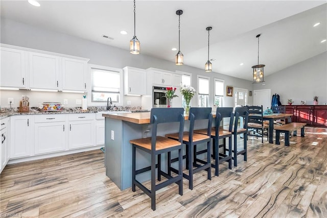 kitchen with pendant lighting, lofted ceiling, white cabinets, a kitchen island, and a breakfast bar area