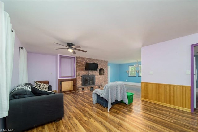 living room featuring a brick fireplace, wood-type flooring, and ceiling fan with notable chandelier