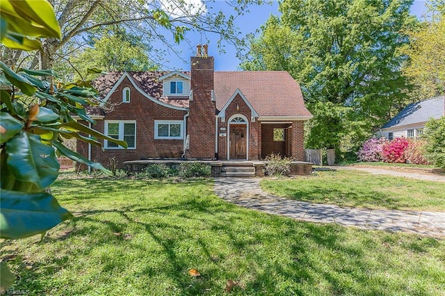tudor home featuring a chimney, brick siding, and a front yard
