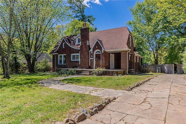 tudor house featuring fence, a front lawn, brick siding, and a chimney