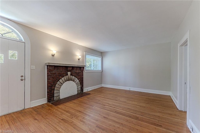 unfurnished living room with light wood-type flooring, a brick fireplace, and baseboards