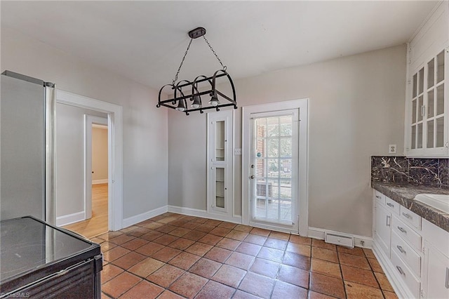 unfurnished dining area featuring baseboards, a notable chandelier, a sink, and light tile patterned floors