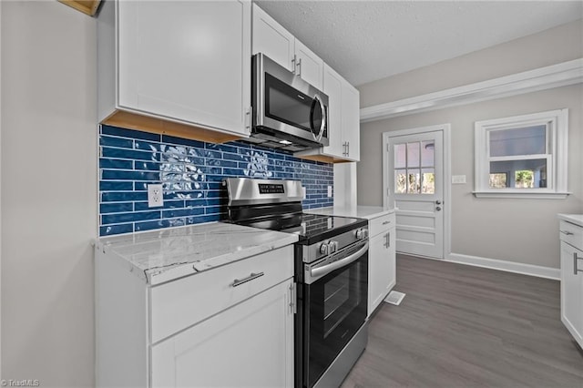 kitchen with dark wood finished floors, backsplash, appliances with stainless steel finishes, white cabinetry, and baseboards