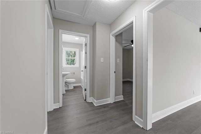 corridor featuring dark wood-type flooring, a textured ceiling, and baseboards