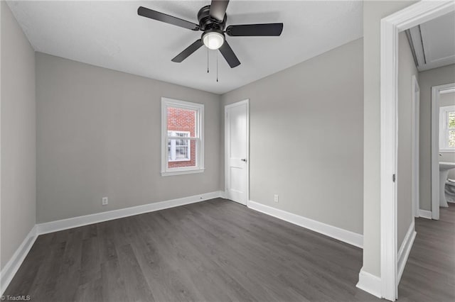 empty room with attic access, a ceiling fan, baseboards, and dark wood-style floors