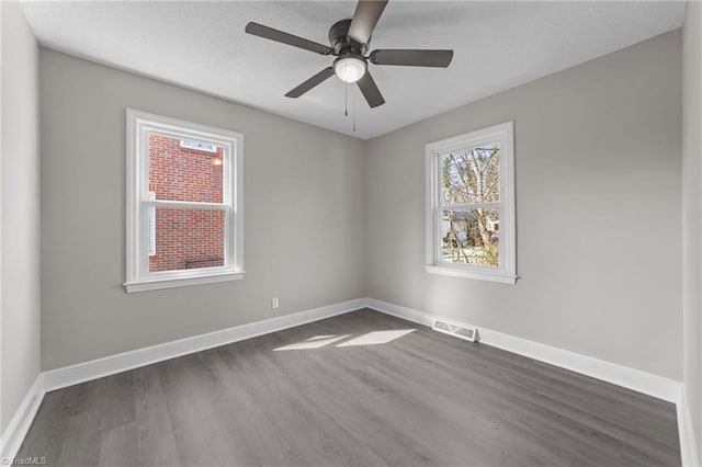 empty room with dark wood-style flooring, visible vents, ceiling fan, and baseboards