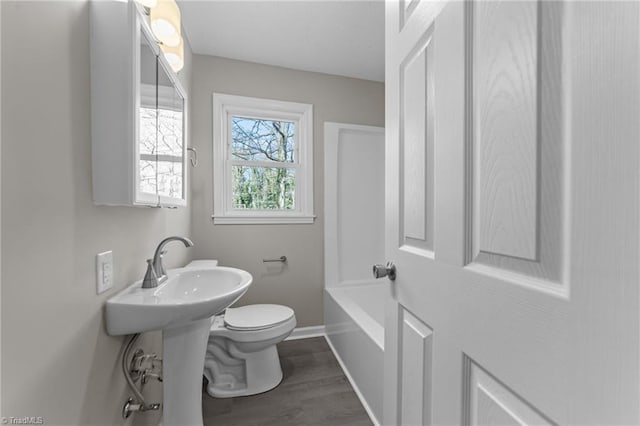 bathroom with a washtub, baseboards, toilet, and wood finished floors