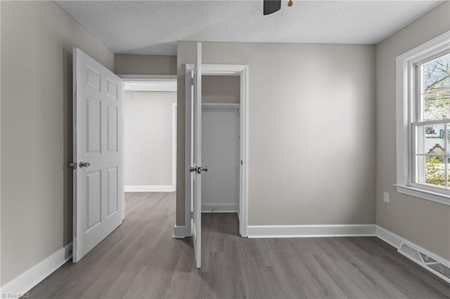 unfurnished bedroom with multiple windows, wood finished floors, visible vents, and baseboards