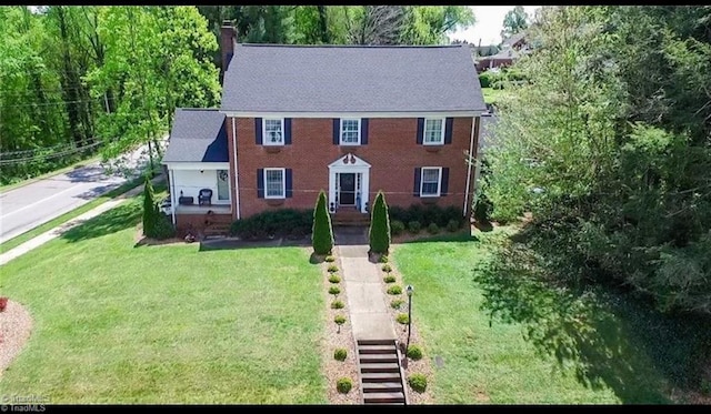 colonial house featuring stairway, brick siding, a chimney, and a front yard