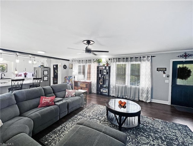 living room with dark wood-type flooring, crown molding, baseboards, and ceiling fan