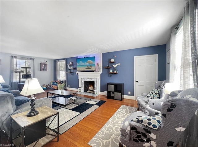living room featuring baseboards, a fireplace with flush hearth, and wood finished floors