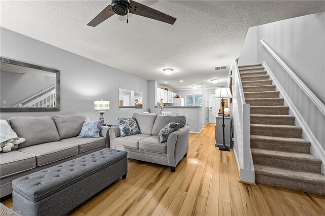 living room featuring ceiling fan, light wood-type flooring, and a textured ceiling