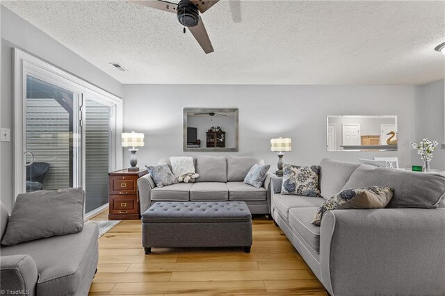 living room with a textured ceiling, light wood-type flooring, and ceiling fan