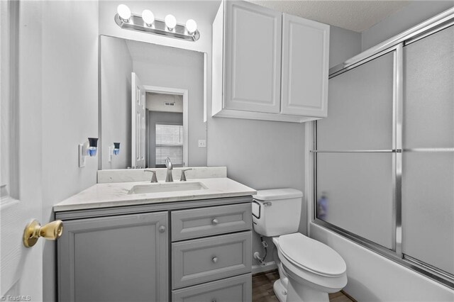 full bathroom with a textured ceiling, vanity, combined bath / shower with glass door, and toilet