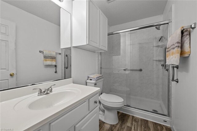 bathroom with a textured ceiling, hardwood / wood-style floors, toilet, an enclosed shower, and vanity