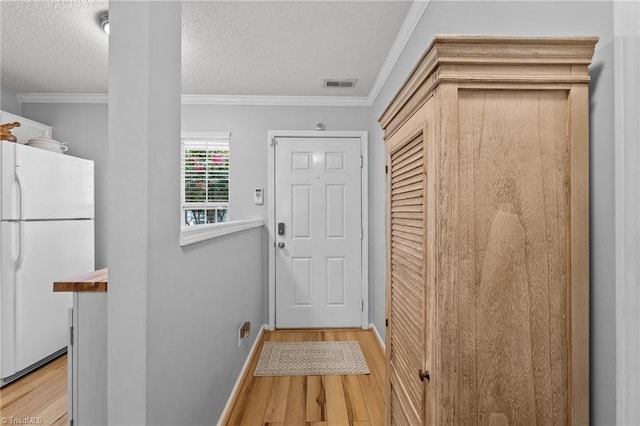 doorway with a textured ceiling, ornamental molding, and light hardwood / wood-style floors