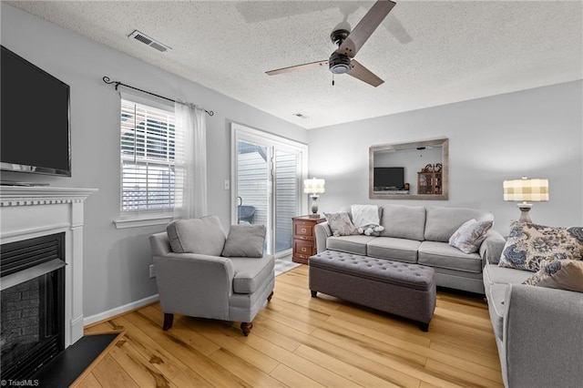 living room featuring ceiling fan, light hardwood / wood-style flooring, and a textured ceiling