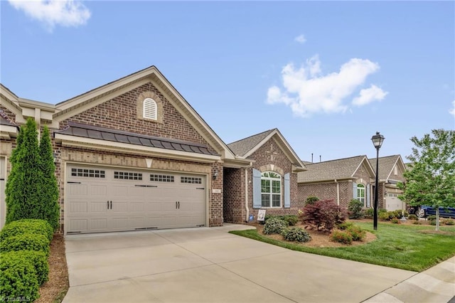 view of front of property with brick siding, driveway, an attached garage, a standing seam roof, and a front lawn