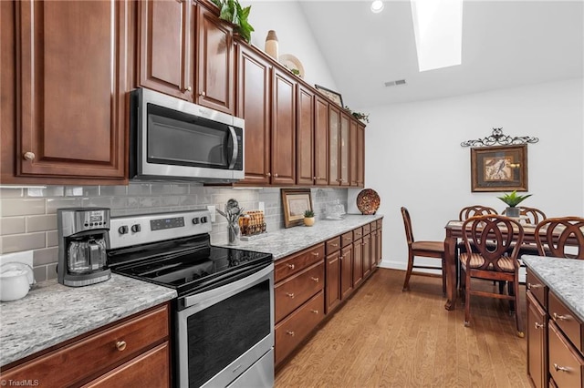 kitchen with stainless steel appliances, vaulted ceiling, a skylight, light wood-type flooring, and tasteful backsplash