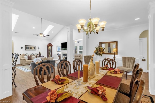 dining space with ceiling fan, wood finished floors, a skylight, lofted ceiling, and arched walkways