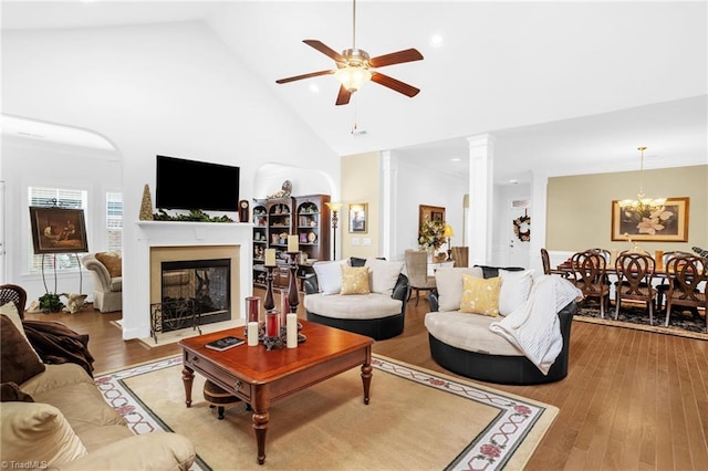 living area featuring high vaulted ceiling, ceiling fan, a fireplace with flush hearth, light wood-type flooring, and decorative columns