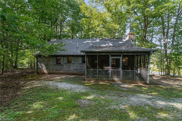 back of house featuring a chimney, a sunroom, and metal roof
