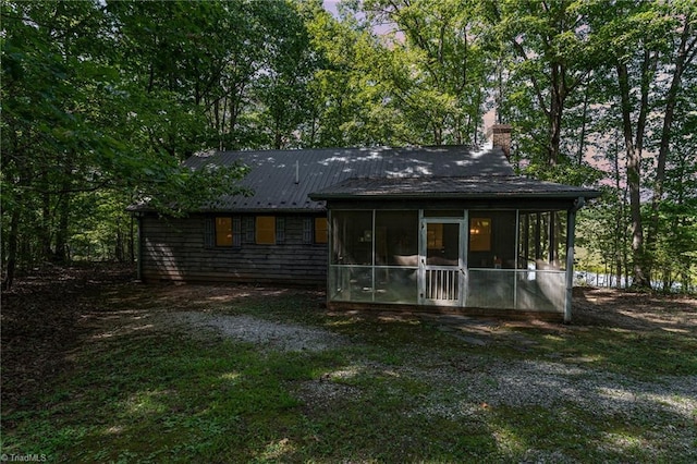 back of property featuring a sunroom, a chimney, and metal roof