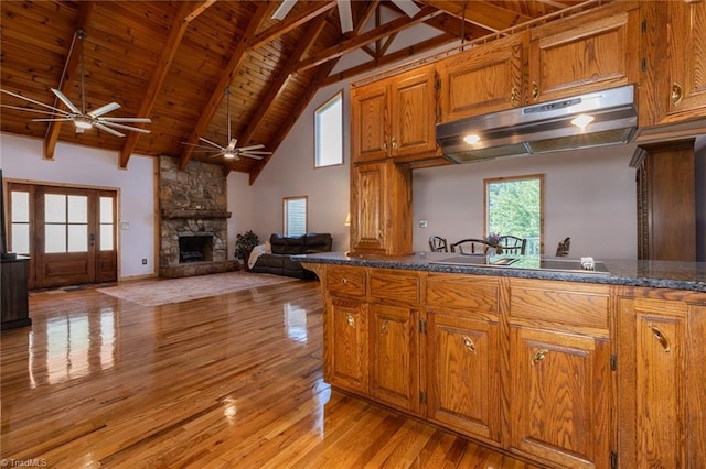 kitchen featuring wooden ceiling, light wood-style flooring, brown cabinets, a stone fireplace, and under cabinet range hood