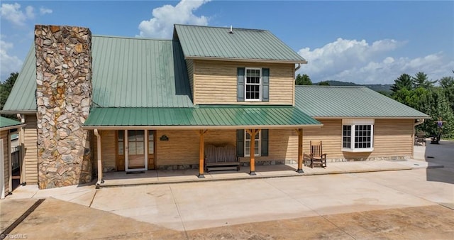 back of property with a porch, metal roof, and a chimney