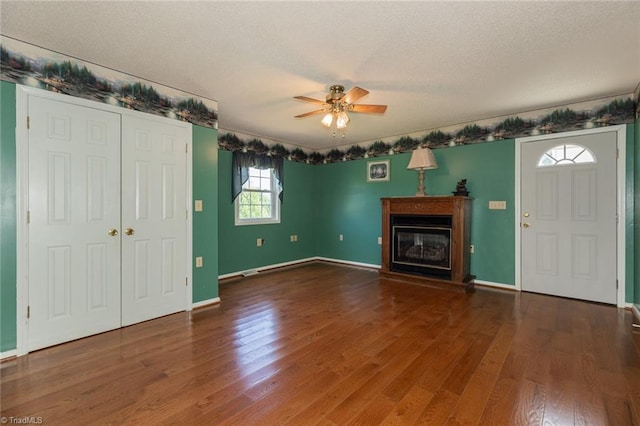 unfurnished living room with baseboards, a glass covered fireplace, ceiling fan, wood finished floors, and a textured ceiling